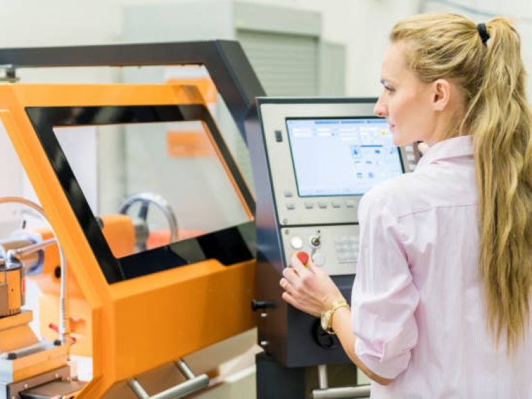 Horizontal color image of pretty woman programming a cnc machine in factory.