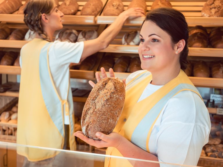 Two salesladies selling bread and other products in bakery shop working as a team